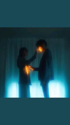 two people standing next to each other in front of a window with light coming from them