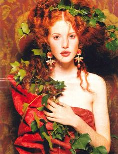 a woman with red hair and green leaves on her head is posing for the camera