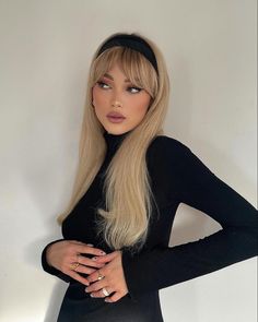 a woman with long blonde hair wearing a black dress and headband standing in front of a white wall