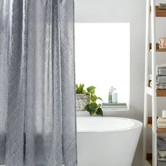 a white bath tub sitting under a window next to a shelf filled with toiletries