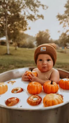 a baby sitting in a metal tub filled with pumpkins