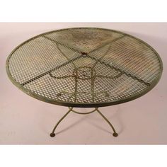 a round metal table with four legs and an iron frame on the top, against a white background