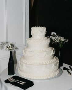 a white wedding cake sitting on top of a table next to two black vases