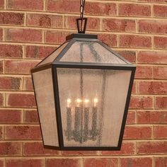 a lantern hanging from the side of a brick wall with five candles lit up on it