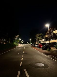 an empty street at night with cars parked on the side