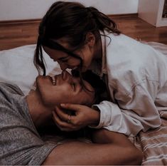 two people are laying on a bed and one is kissing the other's forehead