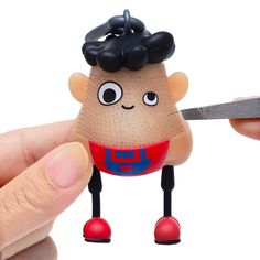 a person holding a pair of scissors in front of a small toy with a face on it