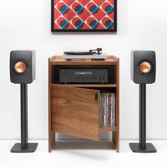 a record player sitting on top of a wooden cabinet next to two speakers and a painting