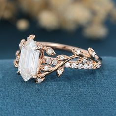 a ring with an emerald stone surrounded by white diamonds on a blue velvet surface next to some flowers