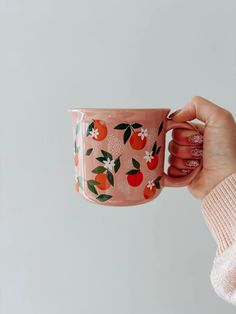 a woman holding a pink coffee cup with oranges on it and flowers painted on the side