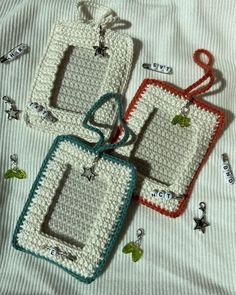 three crocheted tags are sitting on top of a white sheet with green and red trim