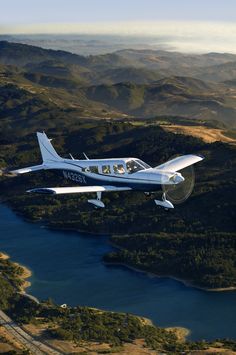 a small plane flying over a lake in the middle of a mountain range with trees