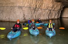 five people in kayaks are paddling through the water near a large cave entrance