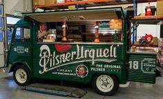 an old fashioned green truck is parked in a garage with shelves and other items behind it