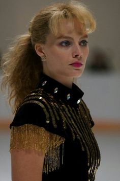 a woman with blonde hair wearing a black top and gold fringes on her shoulders