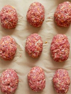 raw meatballs are lined up on a sheet of parchment paper and ready to be cooked