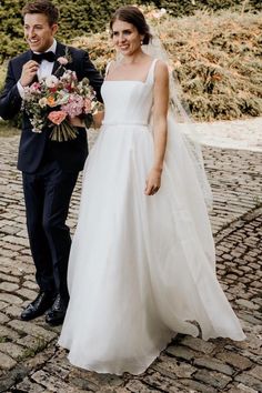 a bride and groom are walking down the cobblestone road together in their tuxedos