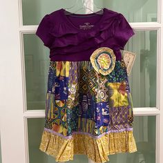 New Handmade Kids Size 4 T-Shirt Dress. The Fabric Motif Is Of Activities At A Fair. A Large Handcrafted Flower Was Placed On The Front Of The Bodice. A Ruffle And Ribbon Was Added To The Bottom Of The Dress. Cute Purple Short Sleeve Dress, Recycled Dress For Kids, Purple Short Sleeve Dress With Patchwork, Purple Patchwork Dress With Short Sleeves, Casual Purple Patchwork Dress, Playful Multicolor Twirl Dress For Play, Purple Patchwork Short Sleeve Top, Purple Short-sleeved Dress With Patchwork, Red Floral Sundress