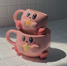 two pink mugs sitting on top of a white tile floor next to each other