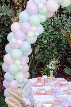 a table topped with lots of balloons next to a lush green bush filled with flowers