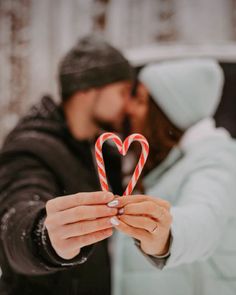 a man and woman holding up a candy cane in the shape of a heart