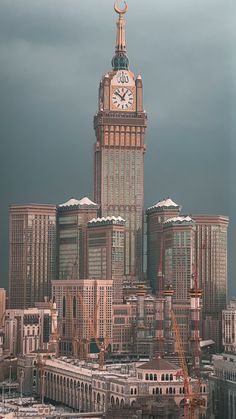 a large clock tower in the middle of a city with tall buildings and cloudy skies