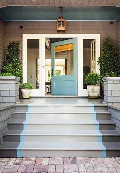 a blue front door with steps leading up to it and potted plants on either side