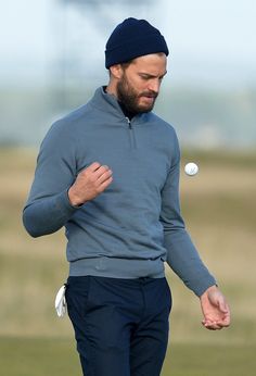 a man with a beard wearing a blue sweater and black pants is throwing a white frisbee in the air