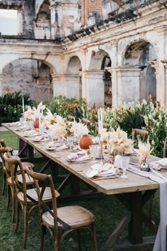 an outdoor table set up with flowers and candles for a wedding reception in front of an old building