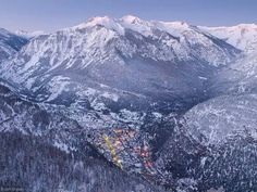 the mountains are covered in snow and there is a town below them with lights on