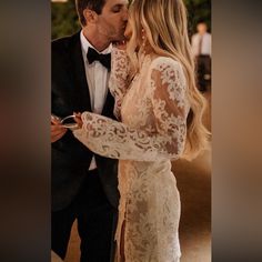 a man in a tuxedo kissing a woman in a white dress with long sleeves