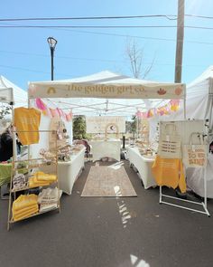 an outdoor market with white tents and yellow towels on the tables in front of it