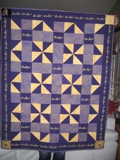 a person holding up a purple and yellow quilt