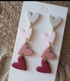 pink and white heart shaped drop earrings with gold accents on the earwires, hanging from a card board