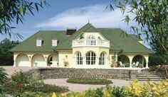 a large house with a green roof and white trim around the windows, surrounded by greenery