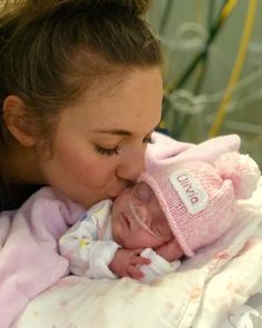 a woman holding a baby in her arms and kissing it's face with the other hand