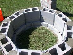 a fire pit made out of cinder blocks in the grass next to an orange bucket