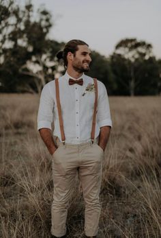 a man standing in the middle of a field wearing suspenders and a bow tie