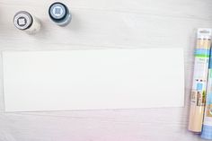 an empty piece of paper next to some crafting supplies on a white wooden surface