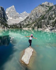 a woman standing on top of a rock in the middle of a lake