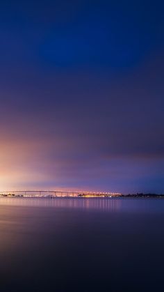 the sky is very dark and cloudy over the water at night with lights in the distance