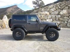 a gray jeep parked in front of a rock wall