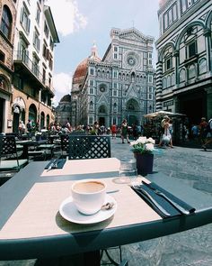 a cup of coffee sitting on top of a table in front of a tall building