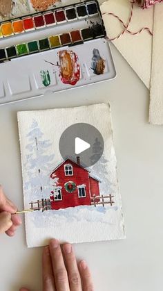 someone is painting a red house on paper with watercolors and paintbrushes