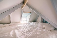 an unmade bed with white sheets and pillows in a lofted room under a slanted ceiling