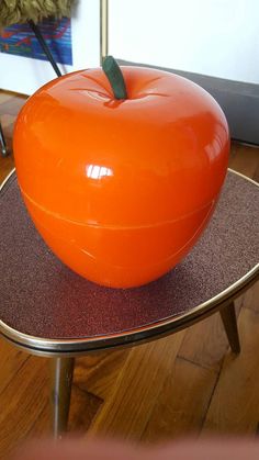 an orange apple sitting on top of a metal stand in front of a wall and floor