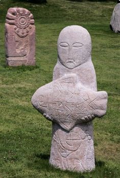 three stone statues sitting in the grass near each other