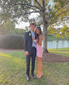 a man and woman standing next to each other in front of a tree on the grass