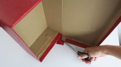 a person holding scissors in front of a box with the lid open and it's inside