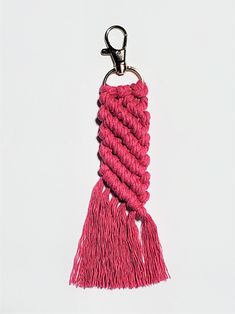 a pink tasseled keychain hanging from a metal hook on a white background